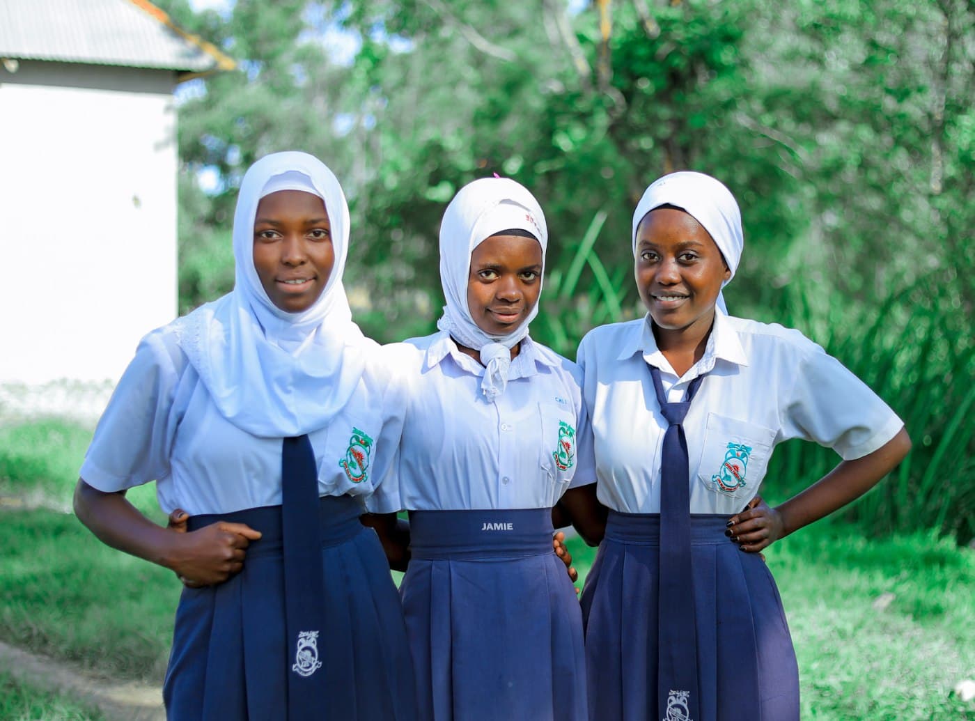 Three schoolgirls in uniform standing proudly outside their school
